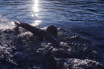 Image showing triathlon athlete swimming on lake in sunrise wearing wetsuit