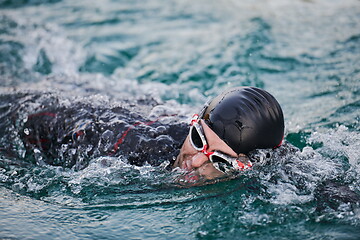 Image showing triathlon athlete swimming on lake in sunrise wearing wetsuit