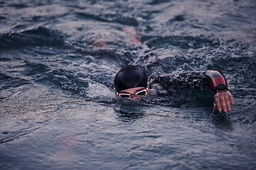 Image showing triathlon athlete swimming on lake in sunrise wearing wetsuit