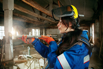 Image showing Woman wearing helmet using male work tools