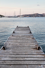 Image showing Wooden pier and sailboats mooring in background at evening calm sea of marvellous Porto Rafael, Costa Smeralda, Sardinia, Italy. Symbol for relaxation, wealth, leisure activity