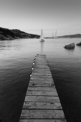 Image showing Wooden pier and sailboats sailing in evening calm sea of marvellous Porto Rafael, Costa Smeralda, Sardinia, Italy. Symbol for relaxation, wealth, leisure activity