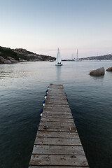 Image showing Wooden pier and sailboats sailing in evening calm sea of marvellous Porto Rafael, Costa Smeralda, Sardinia, Italy. Symbol for relaxation, wealth, leisure activity