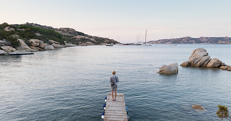 Image showing Beautiful woman in luxury summer dress standing on wooden pier enjoying peaceful seascape at dusk. Vacation, resort and traveling.