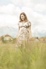 Image showing Beautiful pregnant woman in white summer dress in meadow full of yellow blooming flowers.