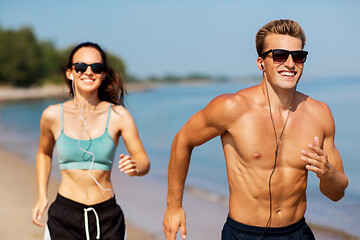 Image showing couple with earphones running along on beach