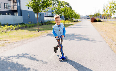 Image showing happy little boy riding scooter in city