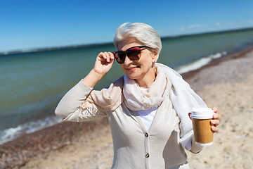 Image showing senior woman drinking takeaway coffee on beach