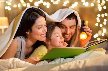 Image showing happy family reading book in bed at night at home