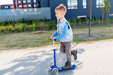 Image showing happy little boy riding scooter in city