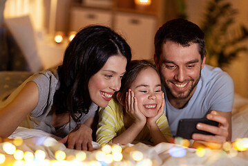 Image showing happy family with smartphone in bed at night