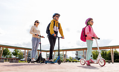 Image showing happy school children with mother riding scooters