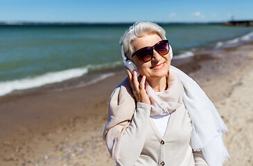 Image showing old woman in headphones listens to music on beach