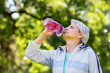 Image showing senior woman drinks water after exercising in park