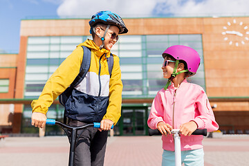 Image showing happy school children in helmets riding scooters