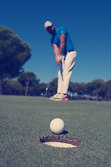 Image showing golf player hitting shot, ball on edge of hole