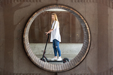 Image showing Casual caucasian teenager riding urban electric scooter in urban environment. Urban mobility concept