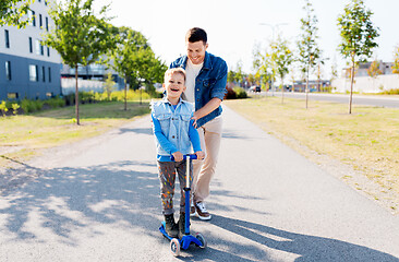 Image showing happy father and little son riding scooter in city