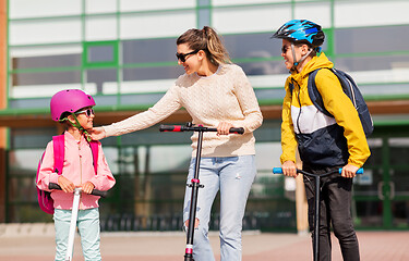 Image showing happy school children with mother riding scooters