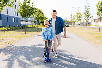 Image showing happy father and little son riding scooter in city