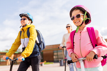 Image showing happy school children with mother riding scooters