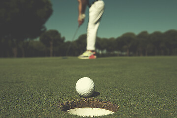 Image showing golf player hitting shot, ball on edge of hole