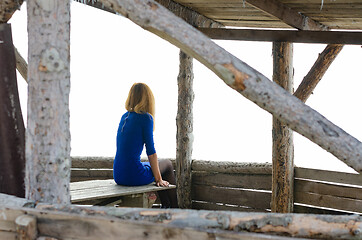 Image showing A girl sits on a table in a gazebo from a log house