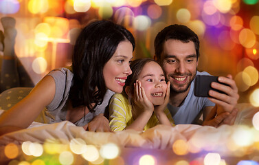 Image showing happy family with smartphone in bed at night