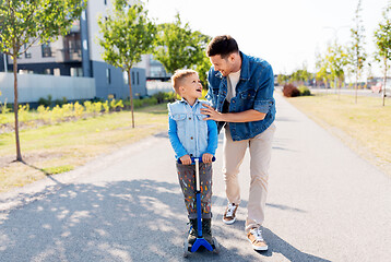 Image showing happy father and little son riding scooter in city