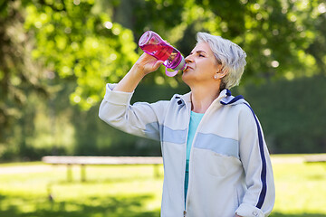 Image showing senior woman drinks water after exercising in park