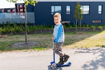 Image showing happy little boy riding scooter in city