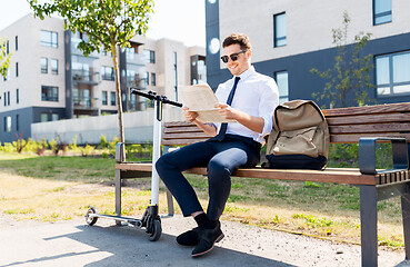 Image showing businessman with scooter reading newspaper in city