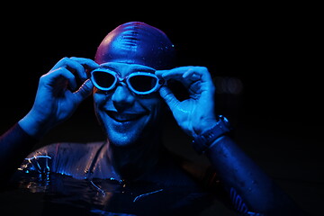 Image showing authentic triathlete swimmer having a break during hard training on night neon gel light