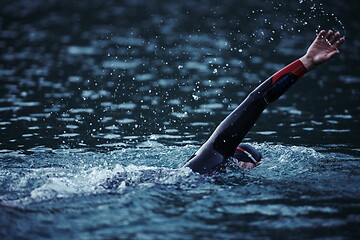 Image showing triathlon athlete swimming on lake in sunrise wearing wetsuit