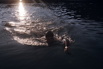 Image showing triathlon athlete swimming on lake in sunrise wearing wetsuit