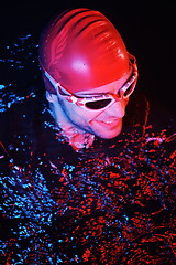 Image showing authentic triathlete swimmer having a break during hard training on night neon gel light