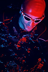 Image showing authentic triathlete swimmer having a break during hard training on night neon gel light