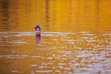 Image showing triathlon athlete swimming on lake in sunrise wearing wetsuit