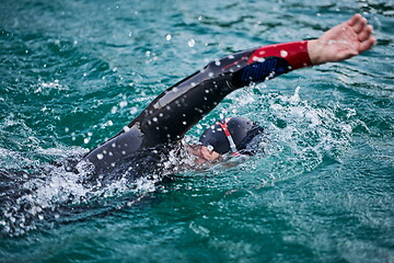 Image showing triathlon athlete swimming on lake in sunrise wearing wetsuit