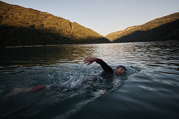 Image showing triathlon athlete swimming on lake in sunrise wearing wetsuit