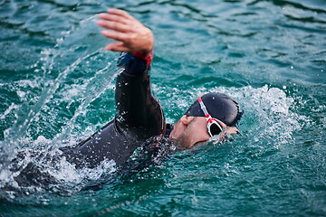 Image showing triathlon athlete swimming on lake in sunrise wearing wetsuit