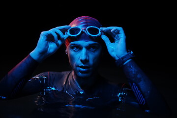 Image showing authentic triathlete swimmer having a break during hard training on night neon gel light