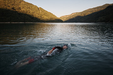 Image showing triathlon athlete swimming on lake in sunrise wearing wetsuit