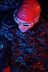 Image showing authentic triathlete swimmer having a break during hard training on night neon gel light