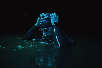 Image showing authentic triathlete swimmer having a break during hard training on night neon gel light