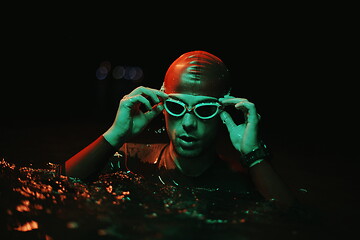 Image showing authentic triathlete swimmer having a break during hard training on night neon gel light