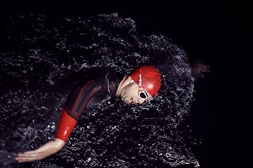 Image showing triathlon athlete swimming in dark night wearing wetsuit