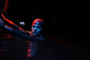 Image showing authentic triathlete swimmer having a break during hard training on night neon gel light