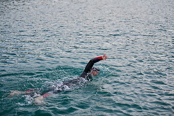 Image showing triathlon athlete swimming on lake in sunrise wearing wetsuit