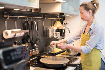 Image showing Stay at home housewife woman cooking in kitchen, stir frying dish in a saucepan, preparing food for family dinner.